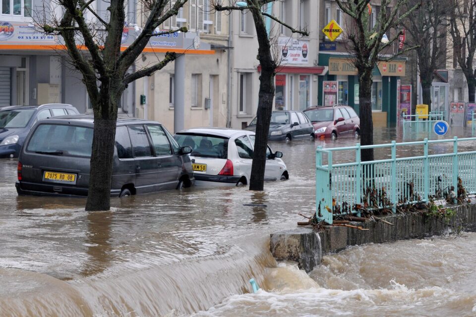 L'image montre une inondation dans les rues de Cherbourg-en-Cotentin, dans la département de la Manche. L'eau a envahie la rue et plusieurs voitures sont coincées.